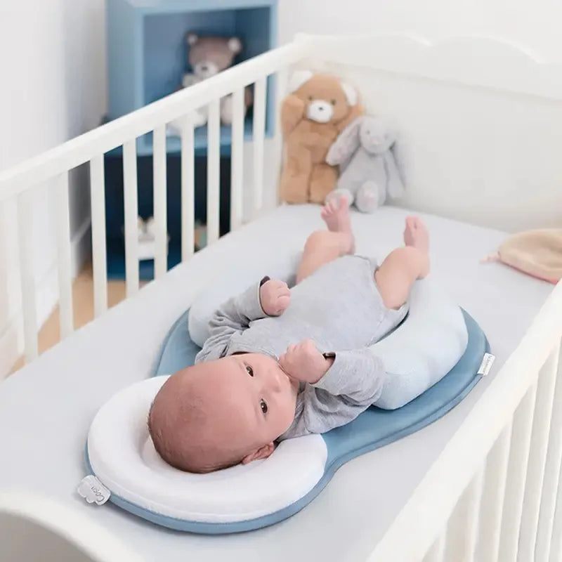 Baby laying in crib on anti rollover pillow  with stuffed toys in white room