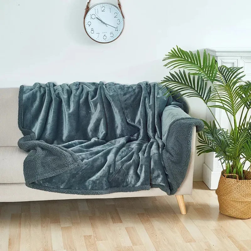 Gray blanket draped over a beige sofa in a living room with a clock and plant in the background.