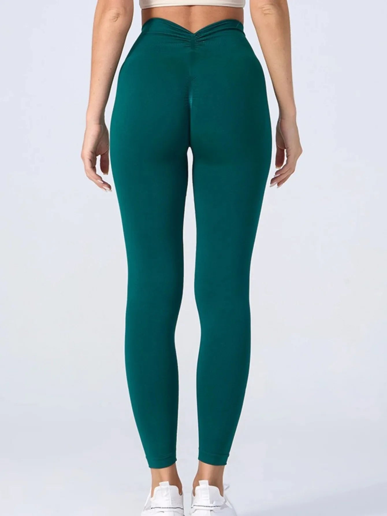 Back view of person wearing green high waist v-back leggings against a neutral background.