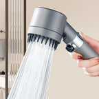 Handheld massaging shower head with water flowing, held by a hand against a neutral background