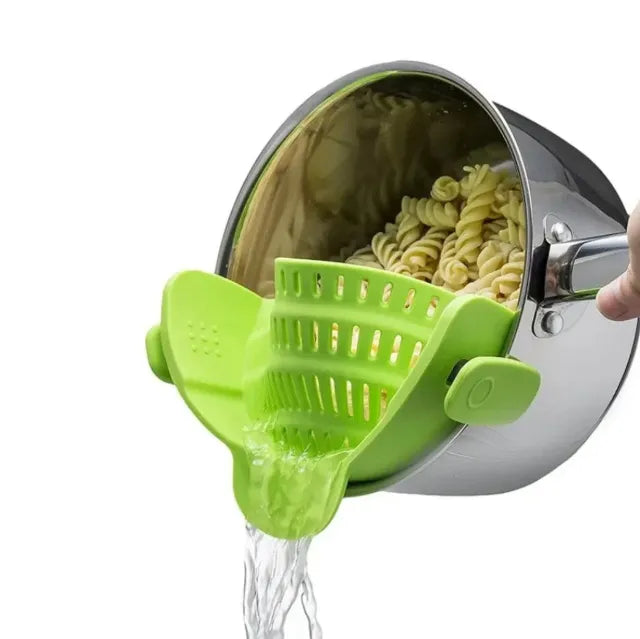 Pasta being drained with a green silicone strainer from a steel pot on white background