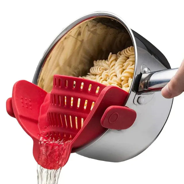 Pasta being drained with a red silicone strainer from a steel pot on white background